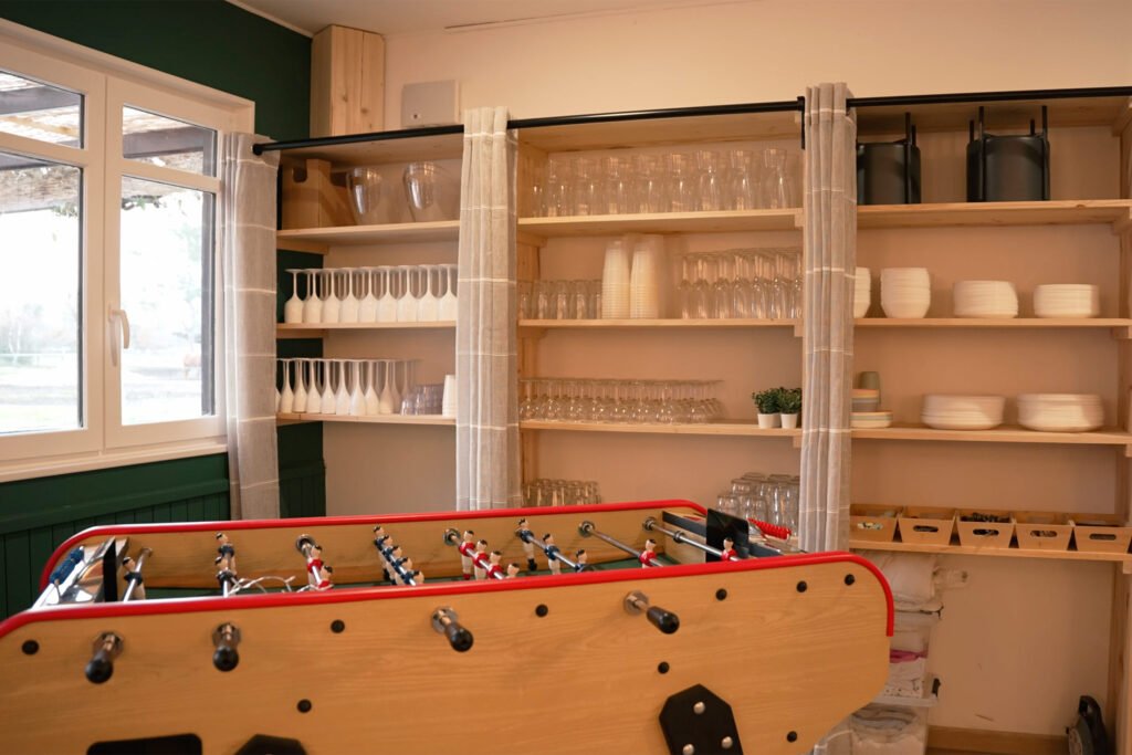 Étagères de rangement avec vaisselle et verres dans le gîte Ranch de Sologne, avec un babyfoot dans l’espace commun.