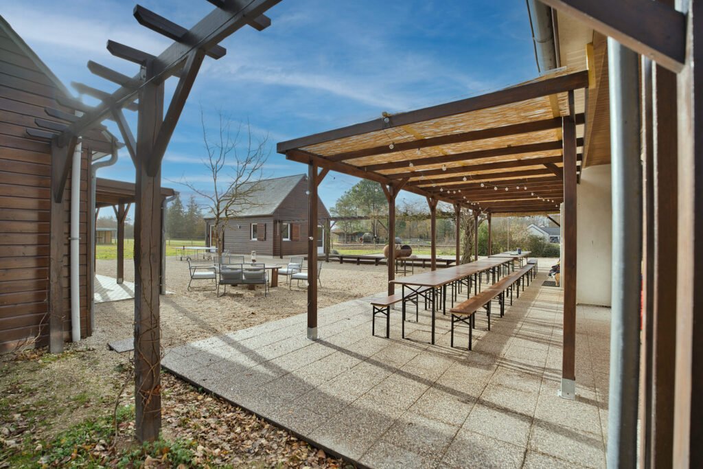 Terrasse extérieure du gîte Ranch de Sologne avec pergola et grandes tables pour les repas en plein air.