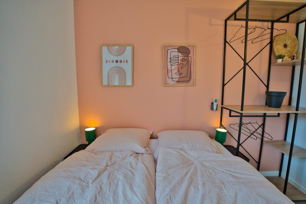 Chambre 7 du gîte Ranch de Sologne avec un lit double, mur rose poudré et étagère dressing en métal noir.